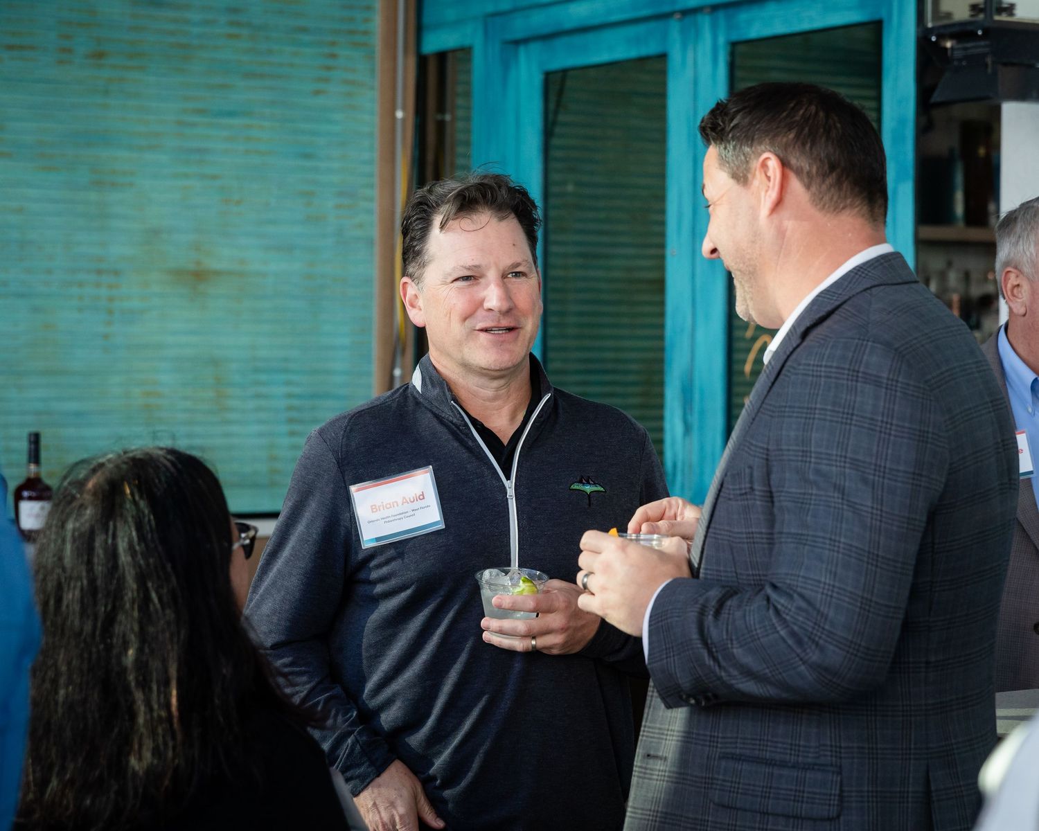 Two businessmen networking at an outdoor event, one holding a drink and wearing a name tag.