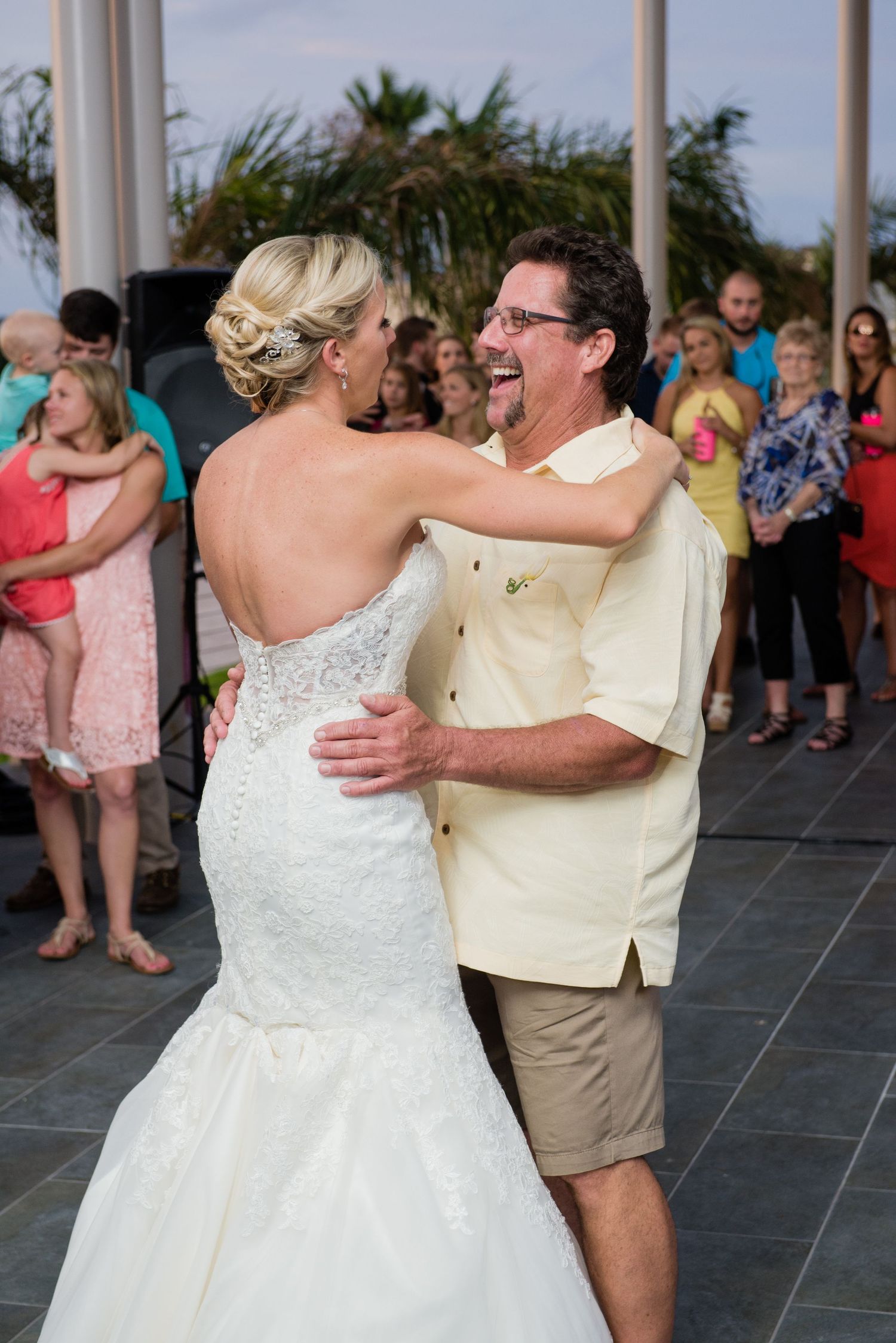 Bride and groom share first dance at outdoor wedding reception with guests watching in background.