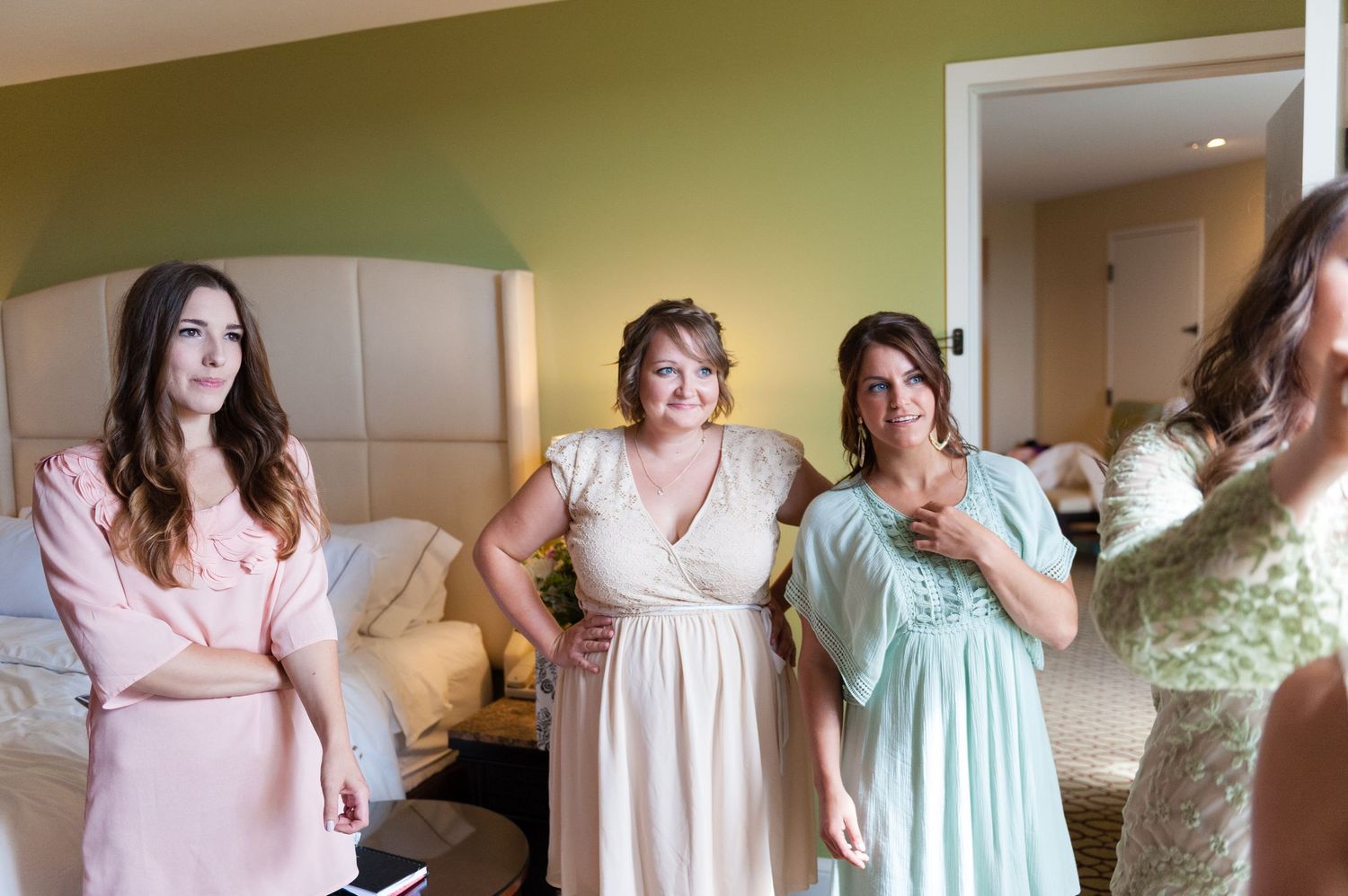 Bridesmaids in pink and mint dresses getting ready together in a hotel room before a wedding ceremony.