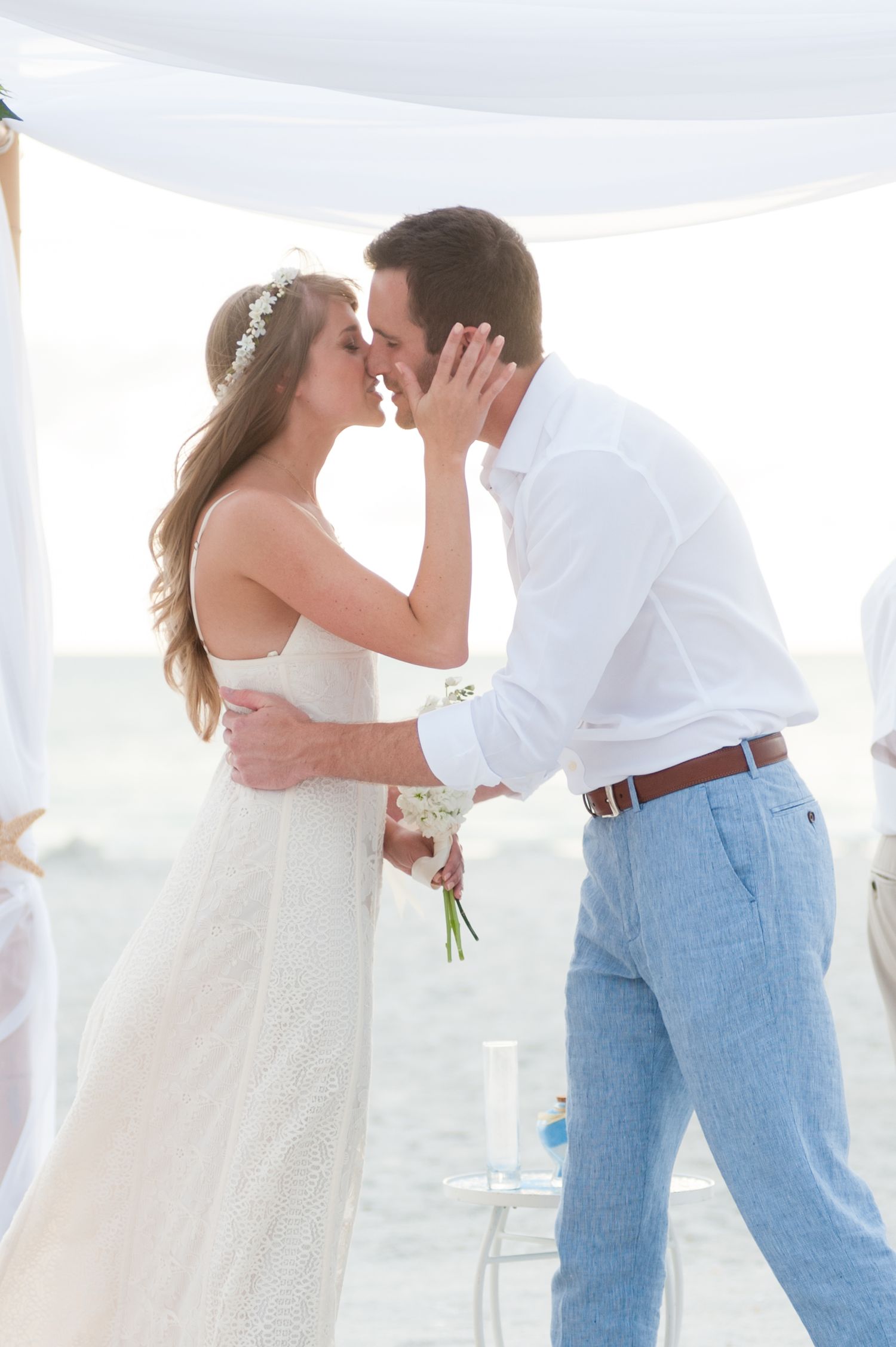 Newlywed couple shares first kiss under white draped canopy on sandy beach on Treasure Island, Florida.