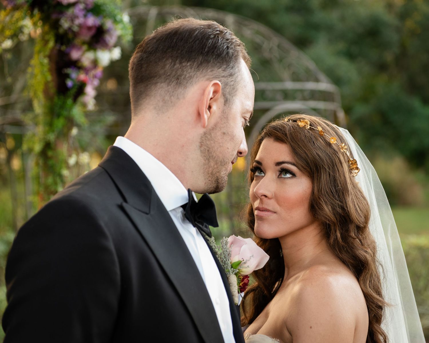 Bride and groom share an intimate moment at outdoor wedding ceremony surrounded by lush floral arrangements.