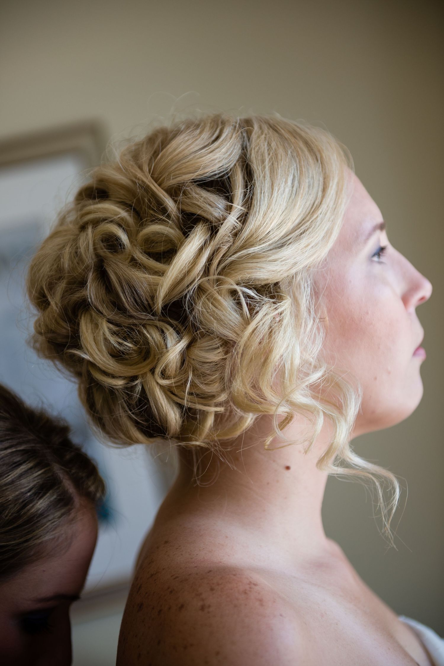 Elegant bridal updo with curly blonde hair styled in a romantic twisted bun, perfect for weddings.