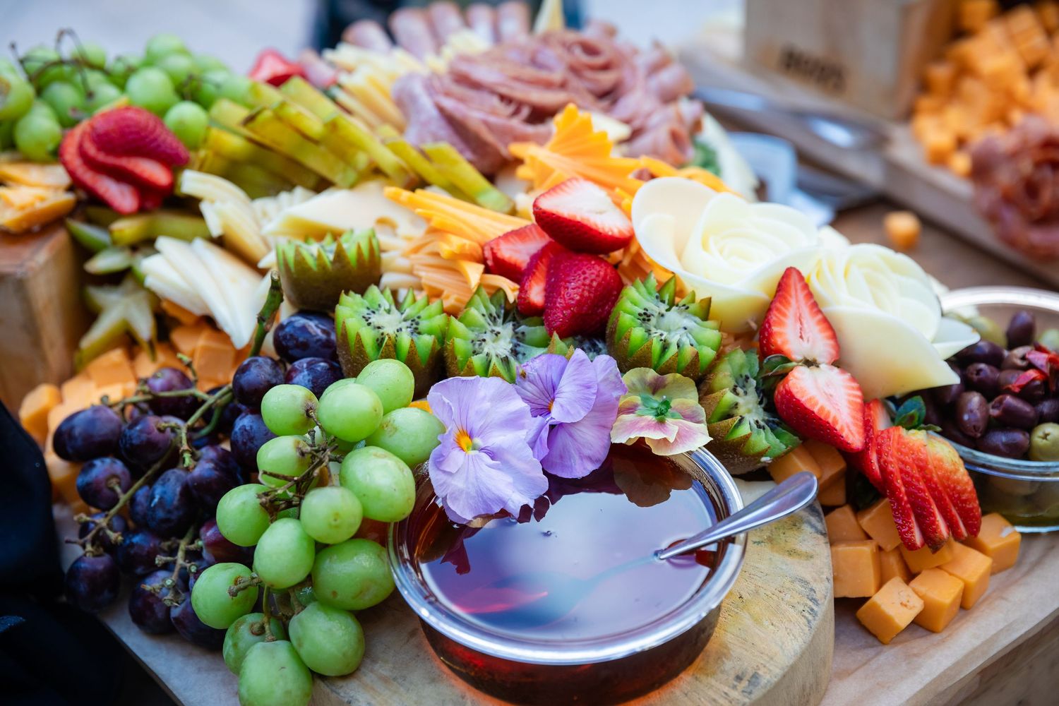 Colorful charcuterie board with fresh fruits, cheeses, and flowers at a catered event.