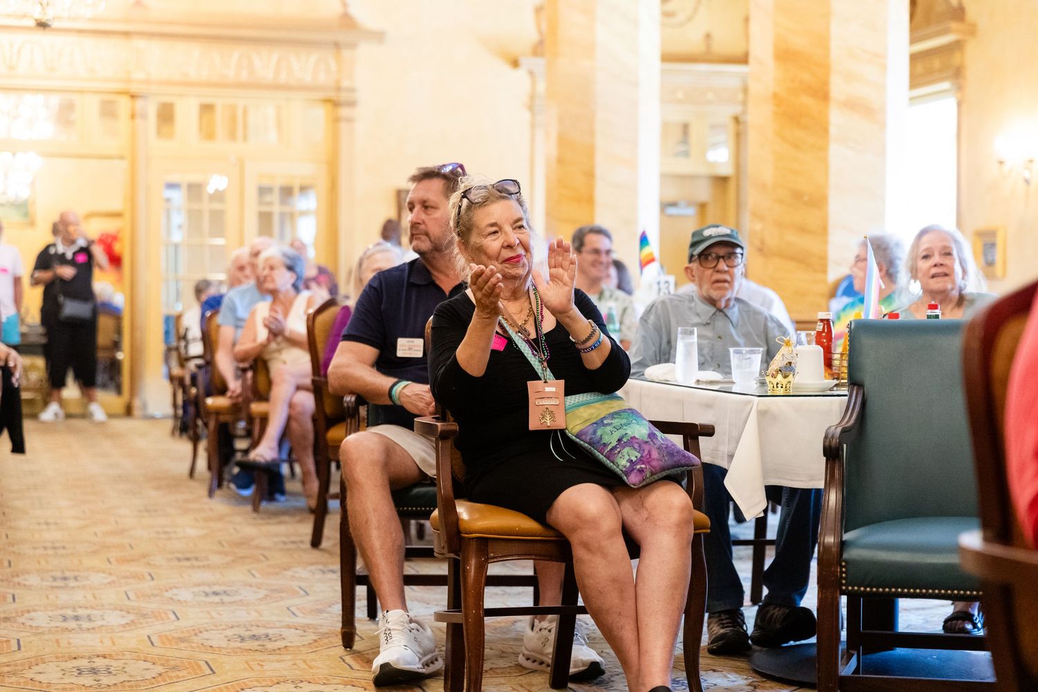 Audience members clap and cheer during a Pride event in an elegant ballroom venue.