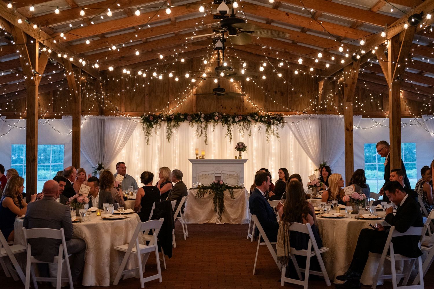 Elegant wedding reception in rustic barn venue with string lights and round tables for guests.
