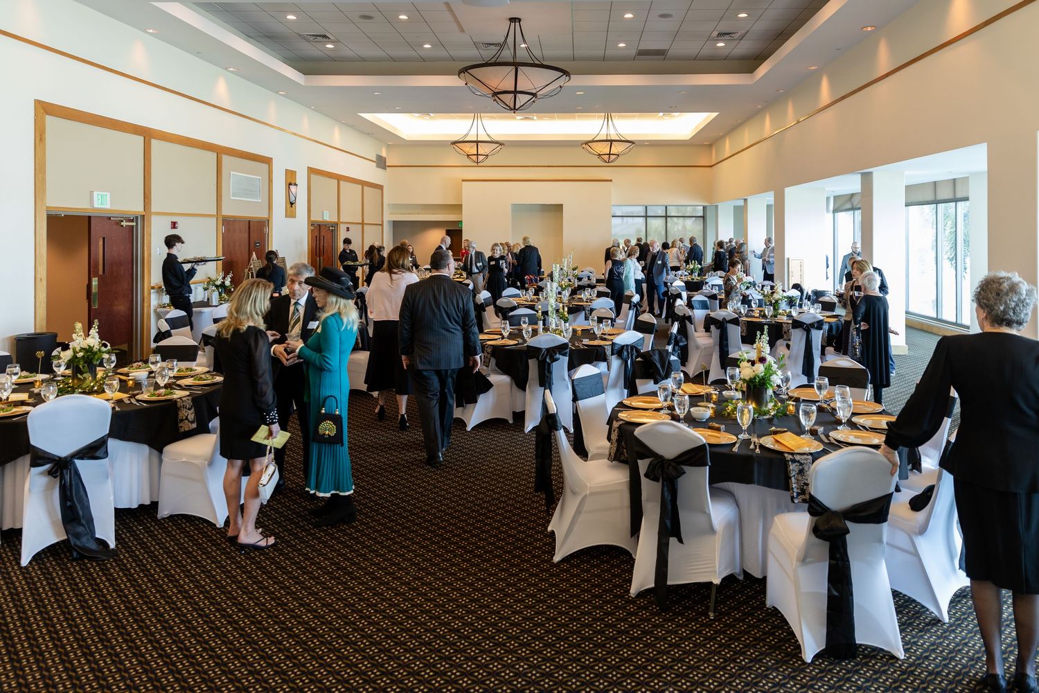 Elegant banquet hall with black and white draped chairs, guests mingling at a formal gala event.