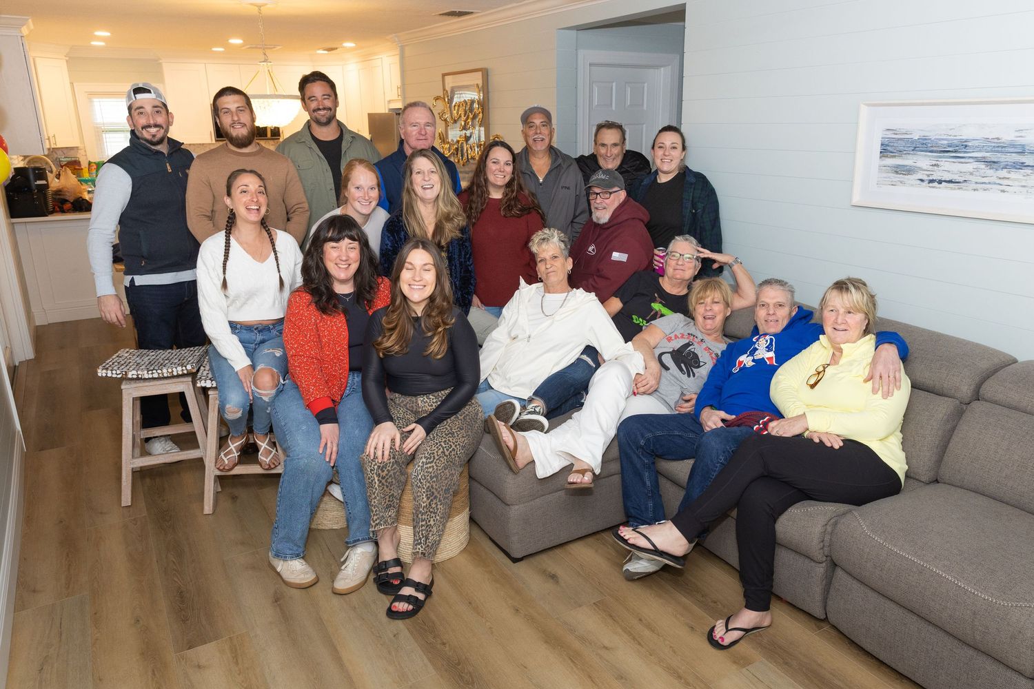 A large group of family members poses together smiling inside a cozy living room.