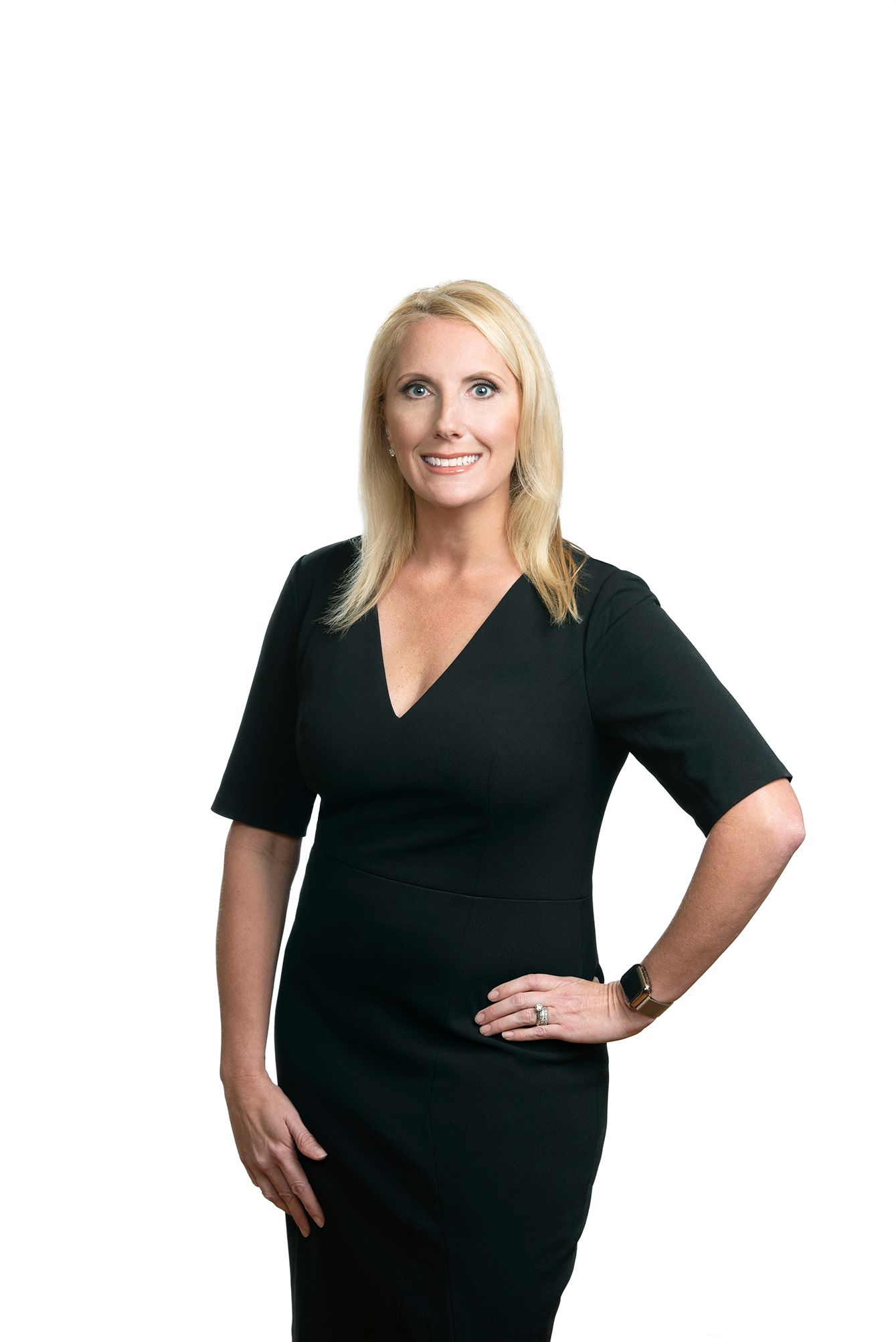 Professional woman in black dress with blonde hair smiling confidently against white background.