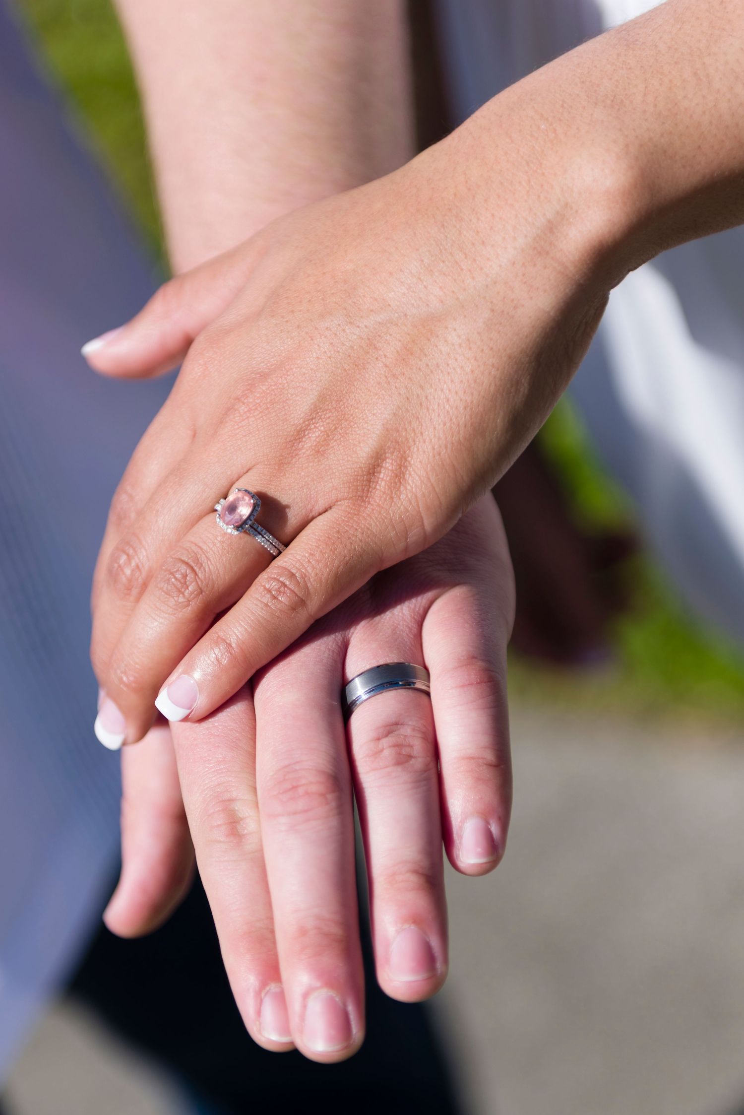 Two newlyweds display their wedding rings, a diamond engagement ring and a simple band, resting their hands together.