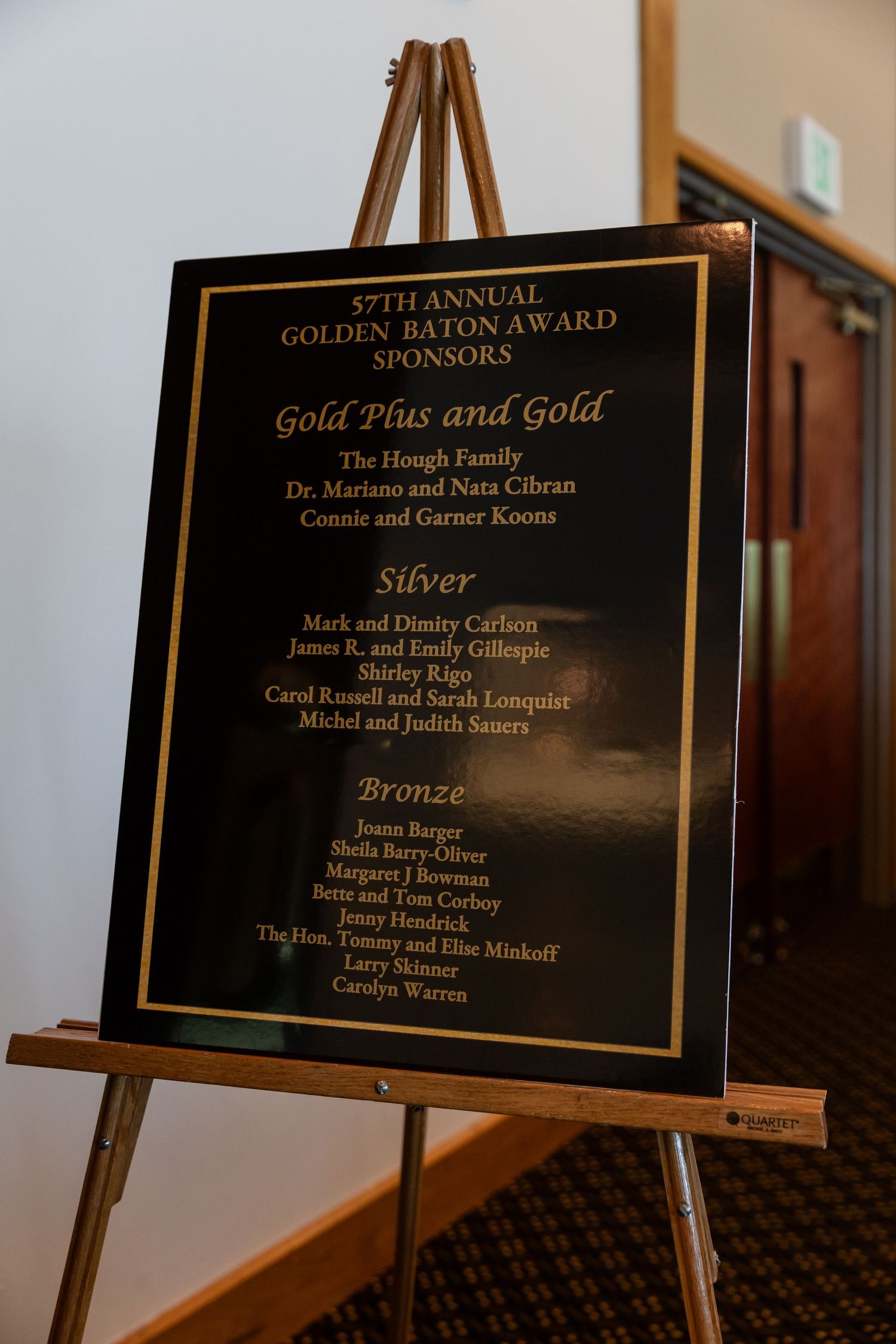 57th Annual Golden Baton Award sponsors board displayed on wooden easel listing Gold, Silver, and Bronze donors.