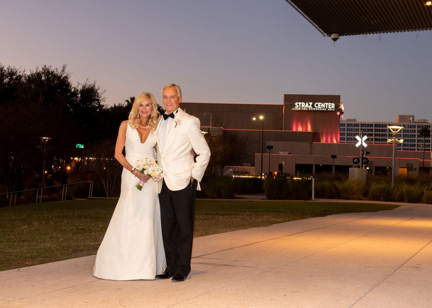 Bride and groom pose outside Straz Center at dusk in Tampa, FL, wearing white gown and tuxedo.