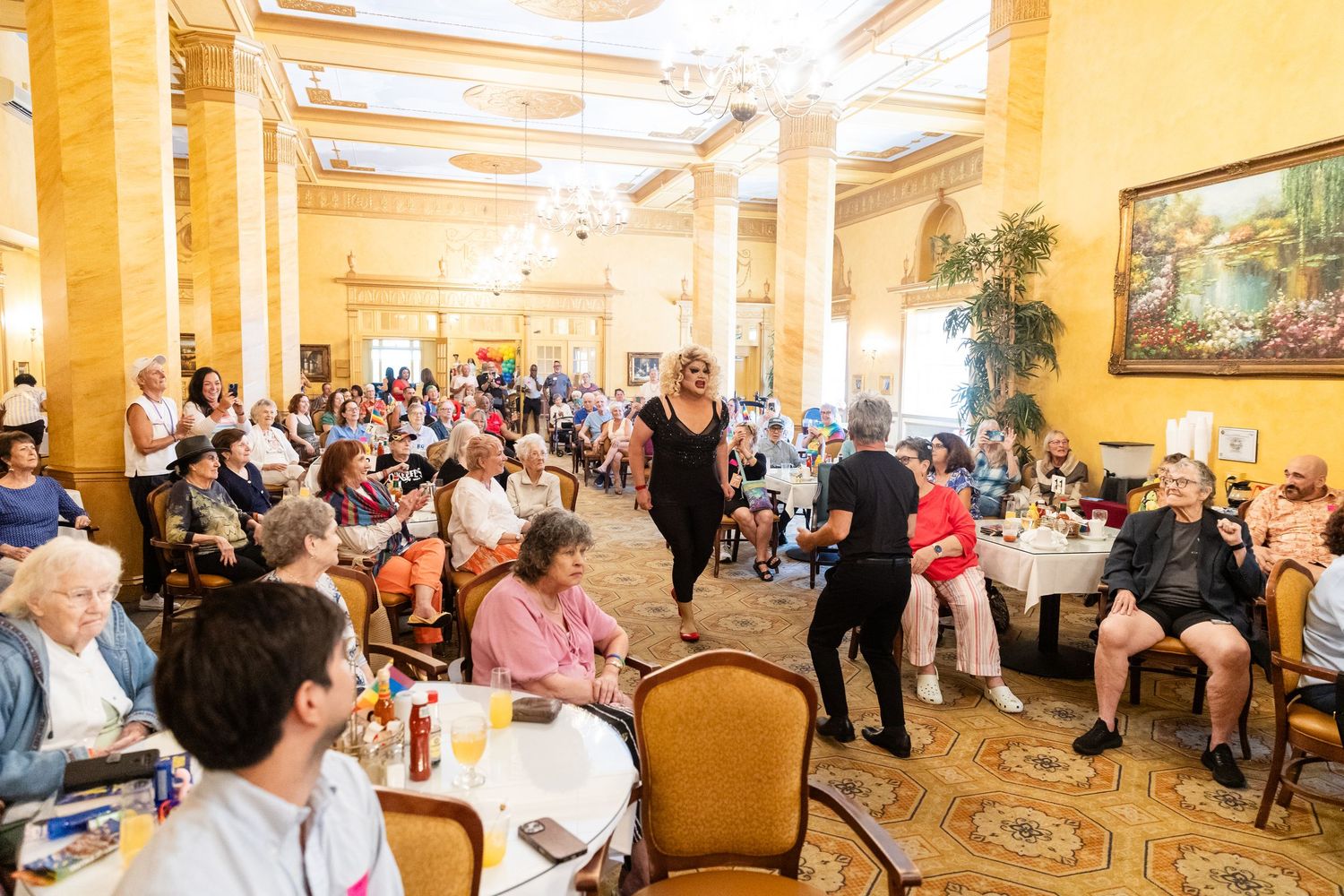 Diverse crowd of guests seated at tables in elegant ballroom watching live performers on the floor.