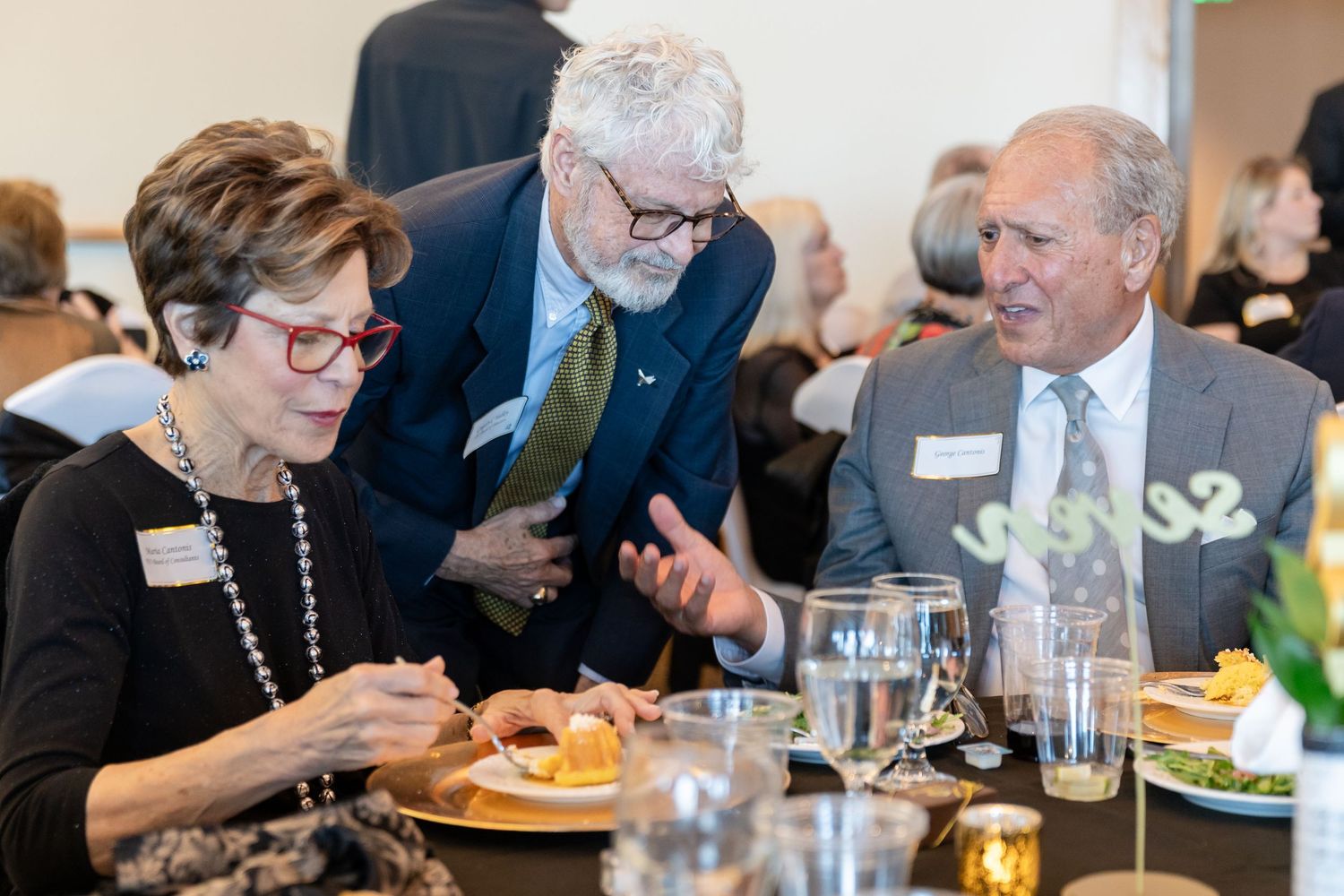 Three professionals networking and conversing at a formal dinner event with food and drinks.