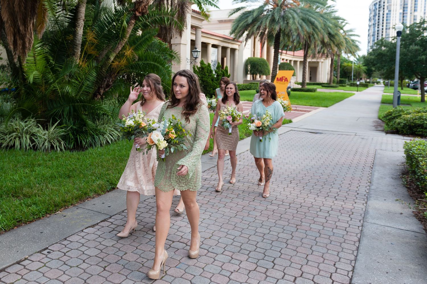Bridesmaids in mint green dresses walking along a brick pathway carrying floral bouquets.