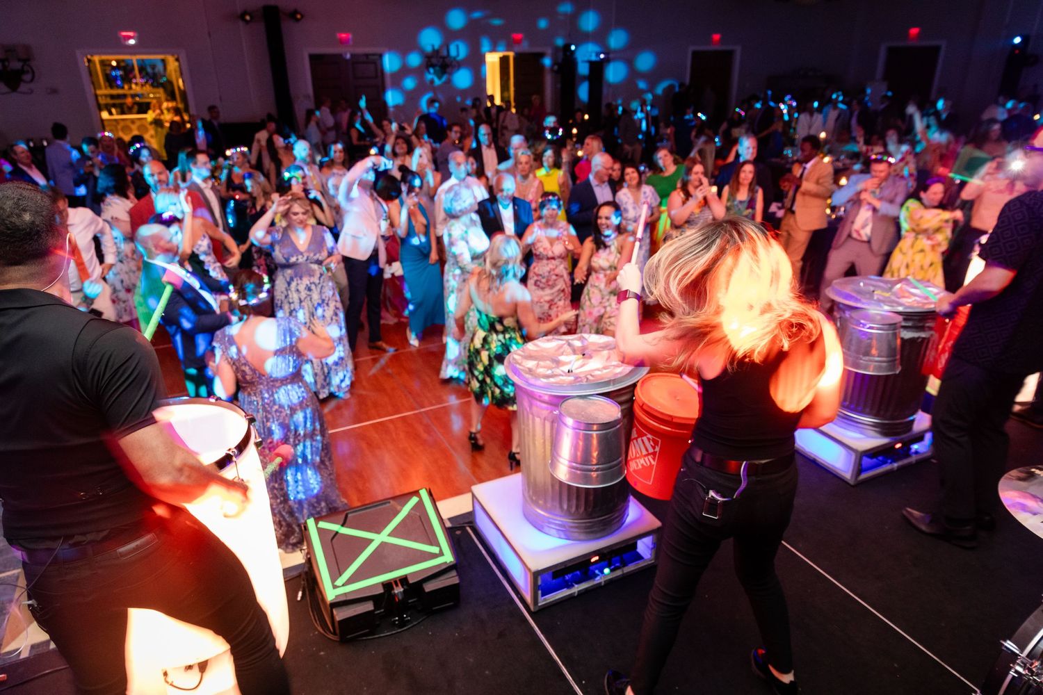 Live drummers perform for a large crowd of formally dressed guests on a packed dance floor at a gala.