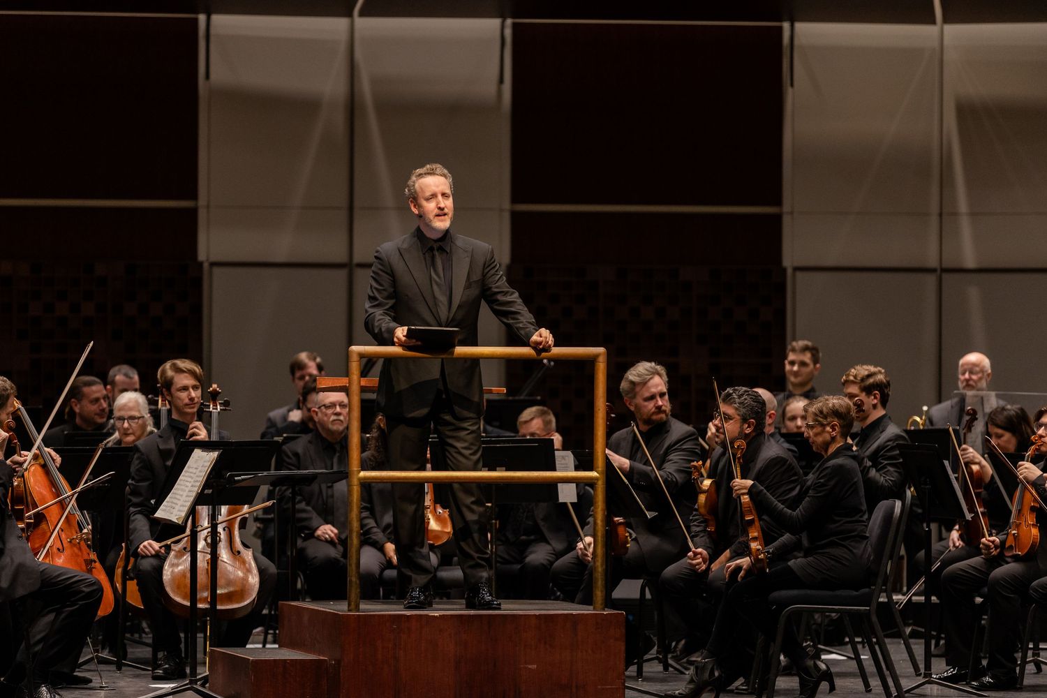 Orchestra conductor leading a full symphony orchestra in a modern concert hall performance.