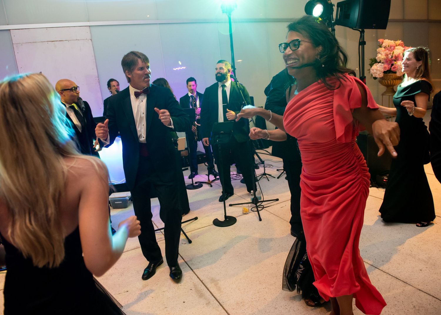 Guests in formal attire dance energetically at an elegant evening gala with a live band.