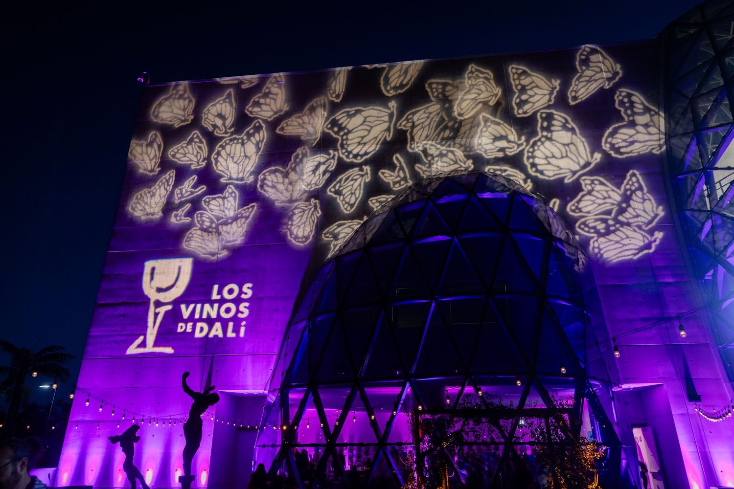 Los Vinos de Dali wine brand building facade lit in purple with butterfly projections at night event.
