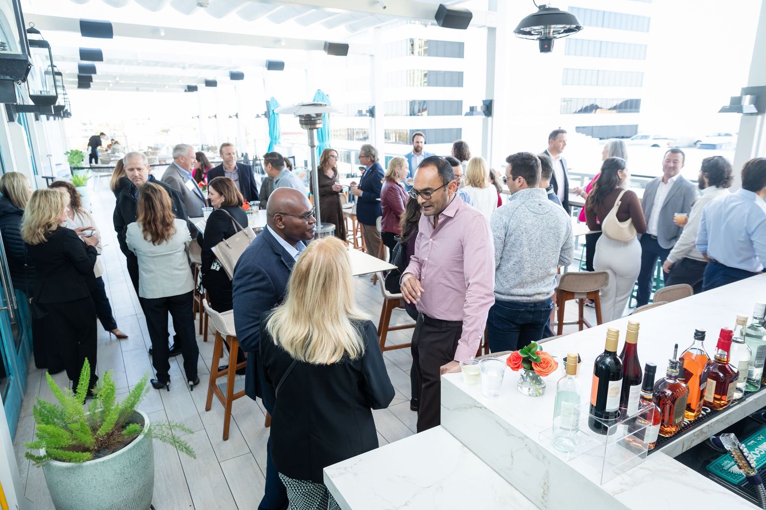 Diverse group of professionals mingling at a busy rooftop bar during a corporate networking event.