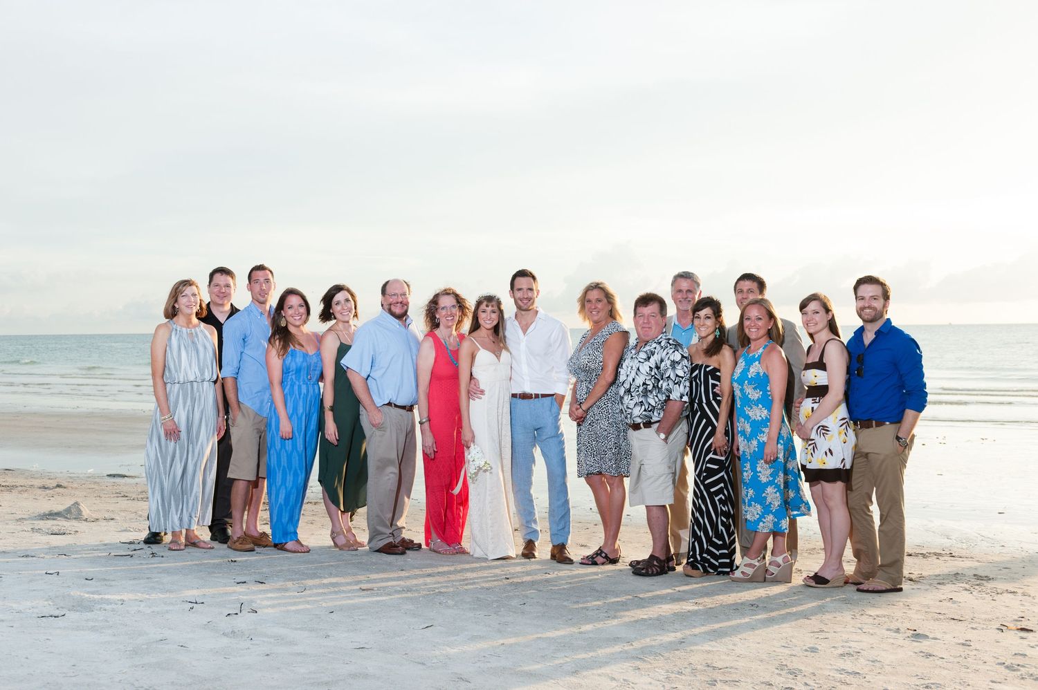 Large family group posing together on a sandy beach at sunset with calm ocean waves in the background.