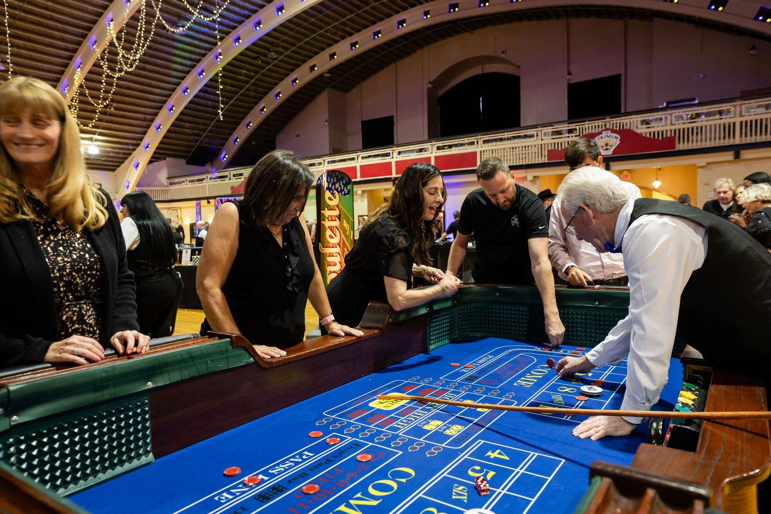 Attendees play craps at a blue casino table during an elegant evening fundraiser event.