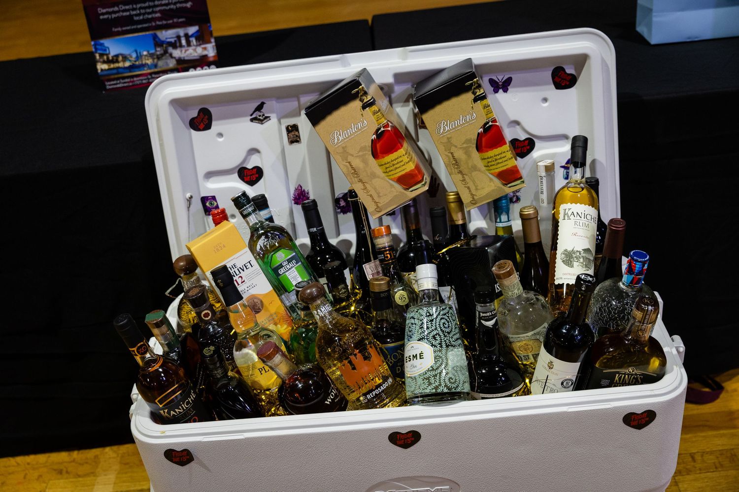 A white cooler filled with assorted liquor bottles and wine, decorated with red hearts at a party event.