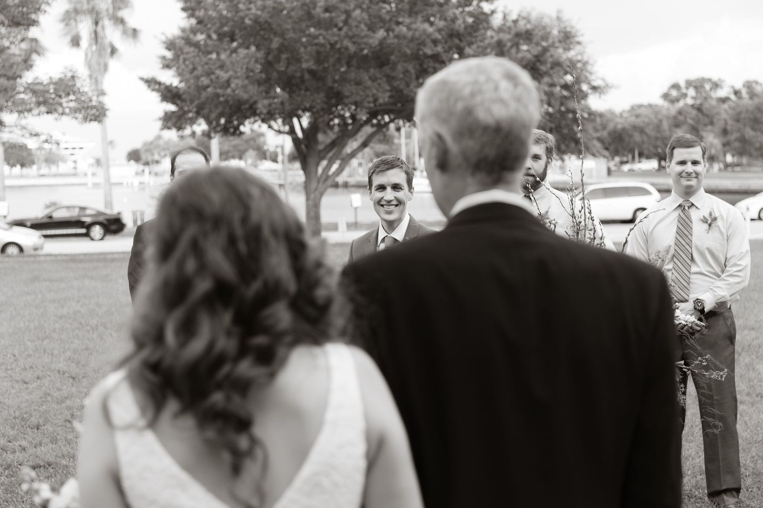 Black and white photo of groom smiling as bride and her father approach during outdoor wedding ceremony Museum of Fine Arts, St. Petersburg.