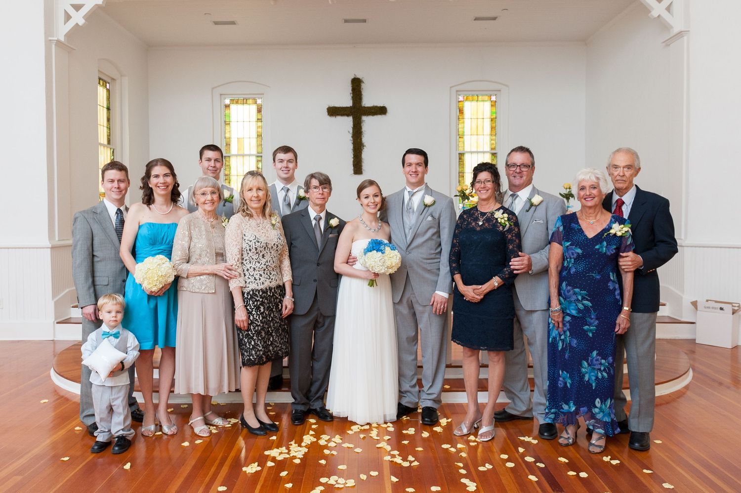Wedding party group photo inside white church with wooden cross.