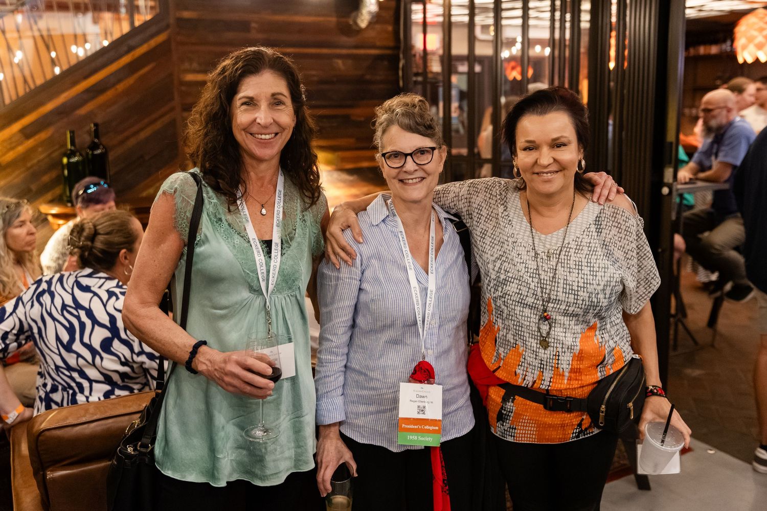 Three women smiling together at an indoor brewery social gathering event.
