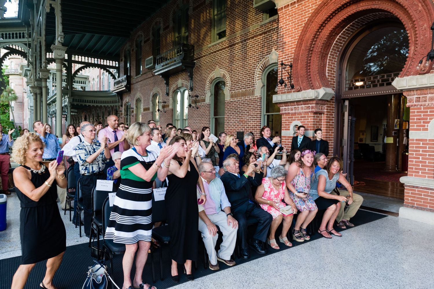 Crowd of guests applauding at an outdoor wedding reception at a historic red brick venue.