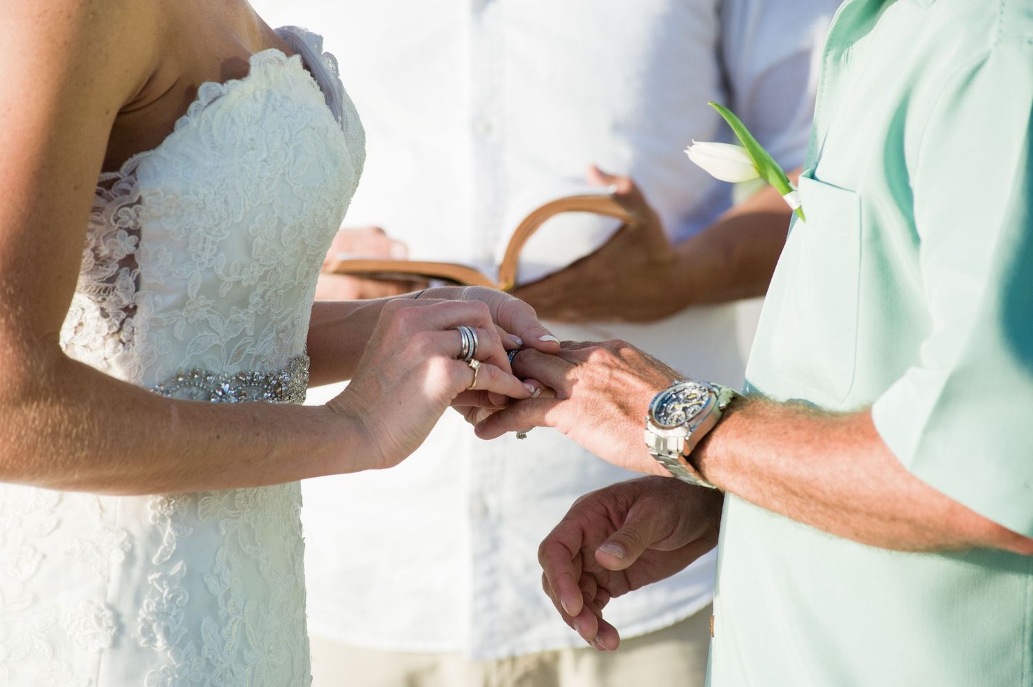 Groom placing wedding ring on brides finger during outdoor beach wedding ceremony exchange of vows.