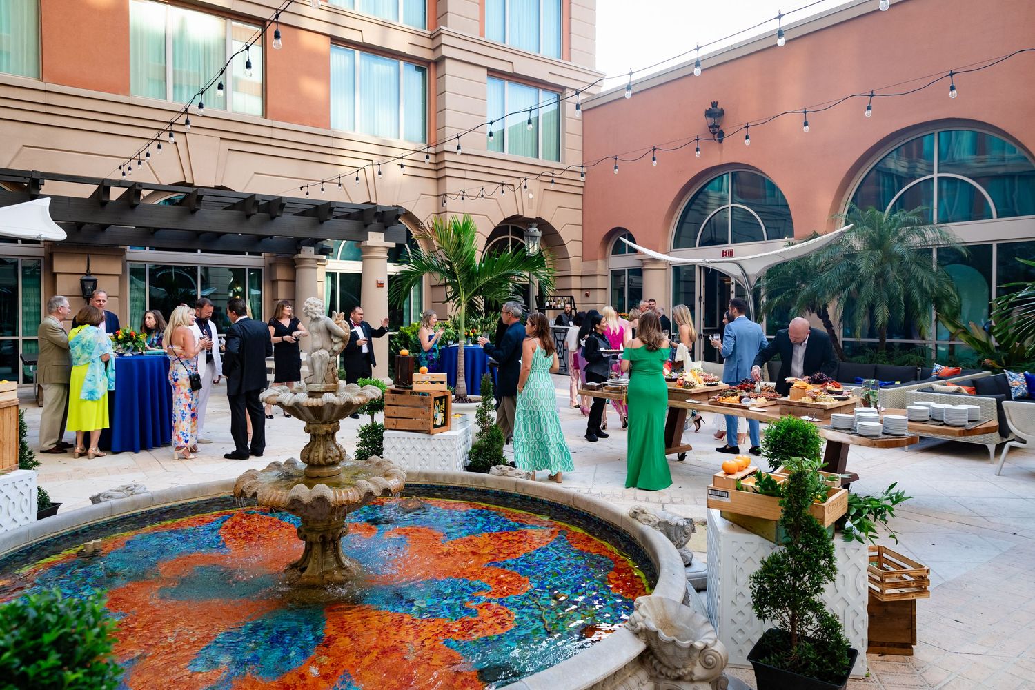 Elegantly dressed guests mingle around a colorful mosaic fountain at an upscale outdoor hotel courtyard reception.
