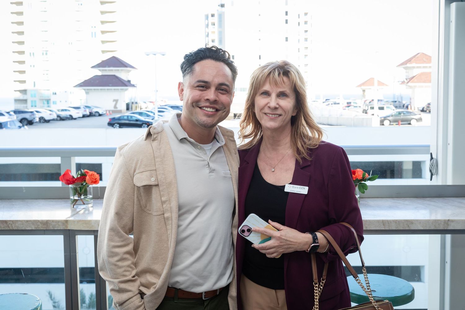 Two professionals smiling together at an outdoor rooftop networking event with city buildings behind them.