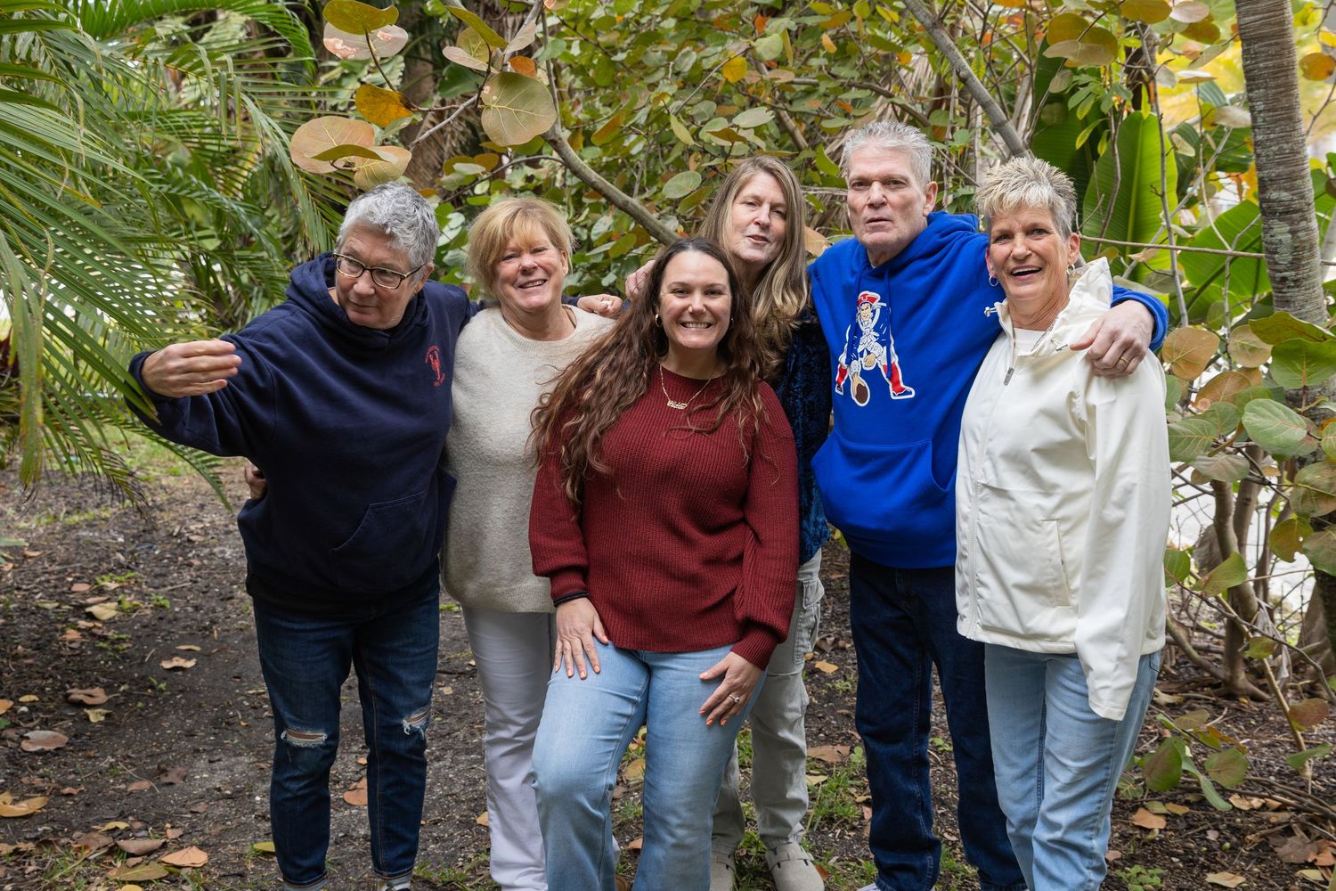 A joyful group of six adults posing together outdoors in a lush tropical garden setting.