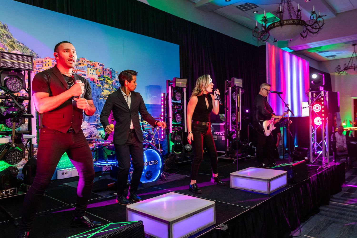 Live band performs on colorful LED-lit stage at elegant event venue with vibrant backdrop.