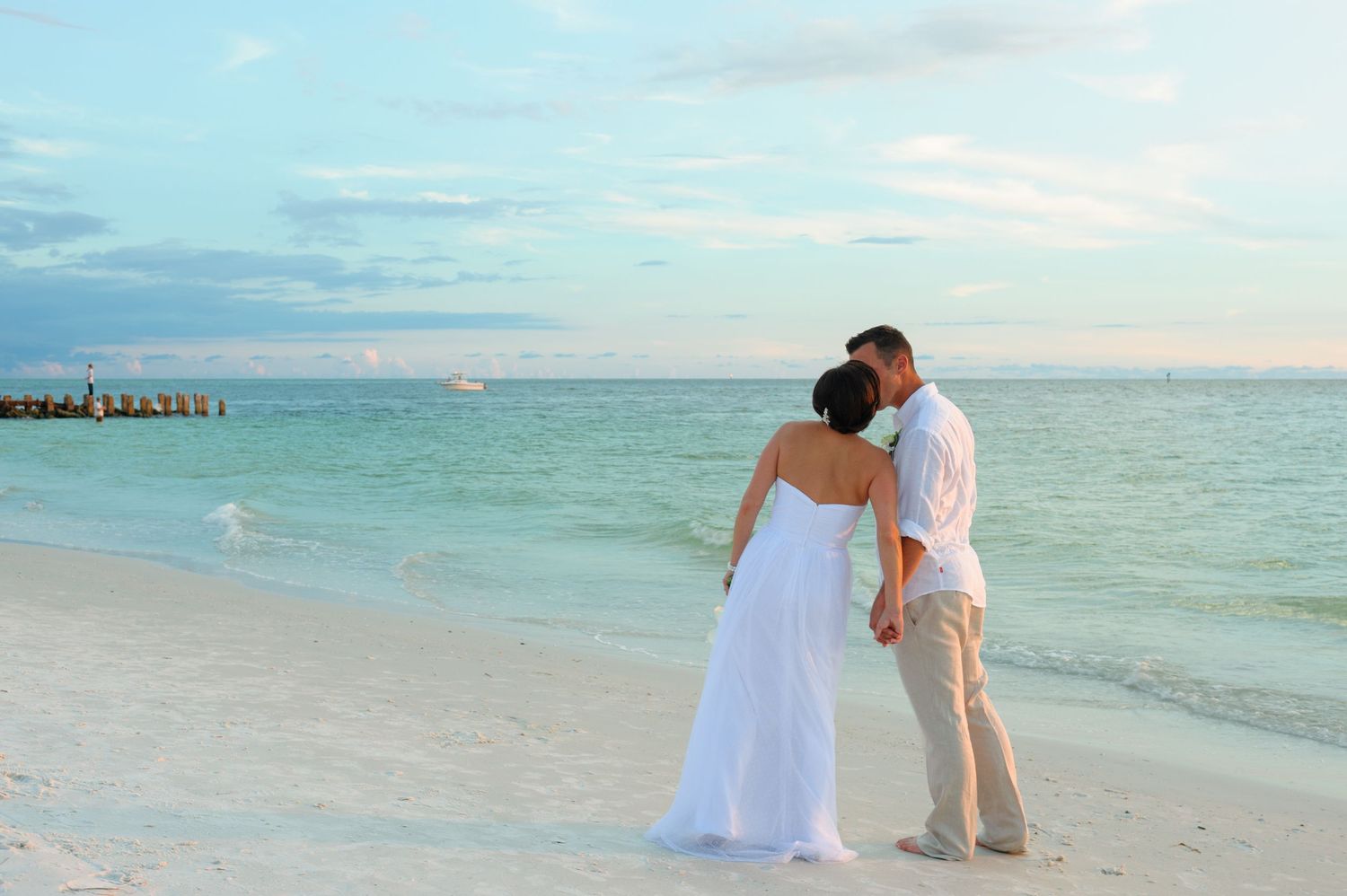 Bride and groom sharing a romantic kiss on a tropical white sand beach at sunset.