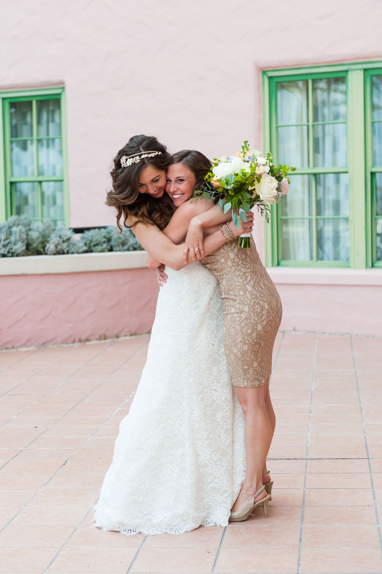 Bride in white lace wedding dress embracing bridesmaid in gold sequin dress while holding bouquet at The Vinoy Resort.