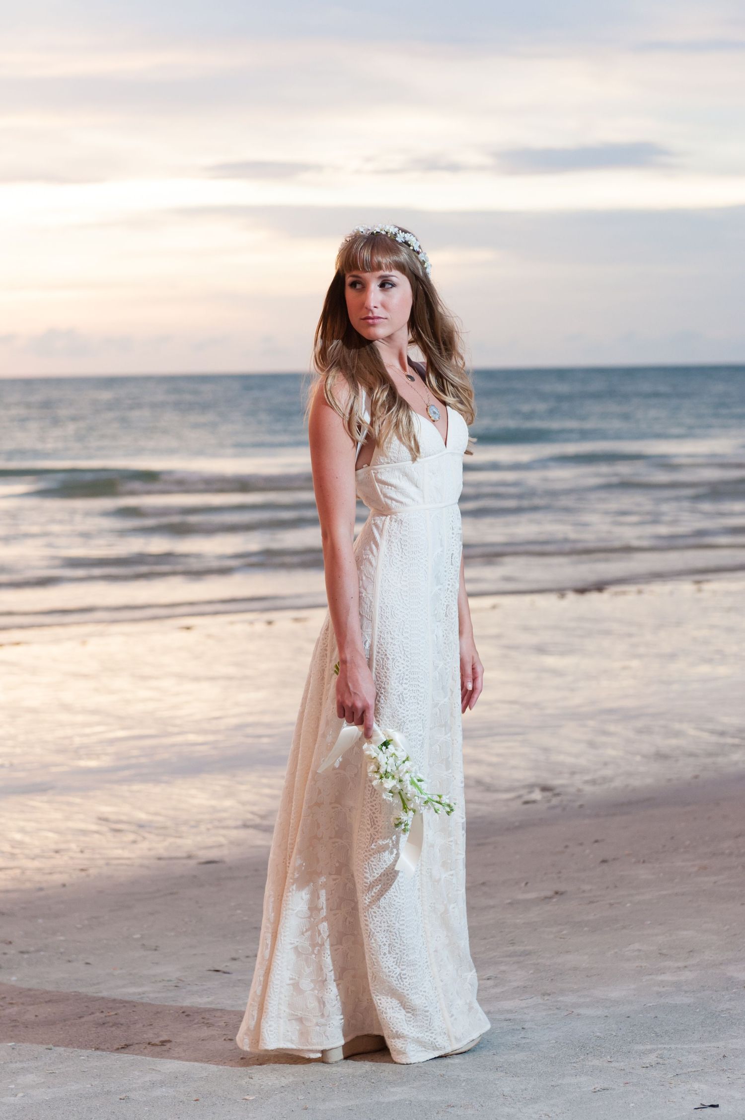 Elegant bride in white lace gown holds bouquet at sunset on the beachon Treasure Island, Florida.