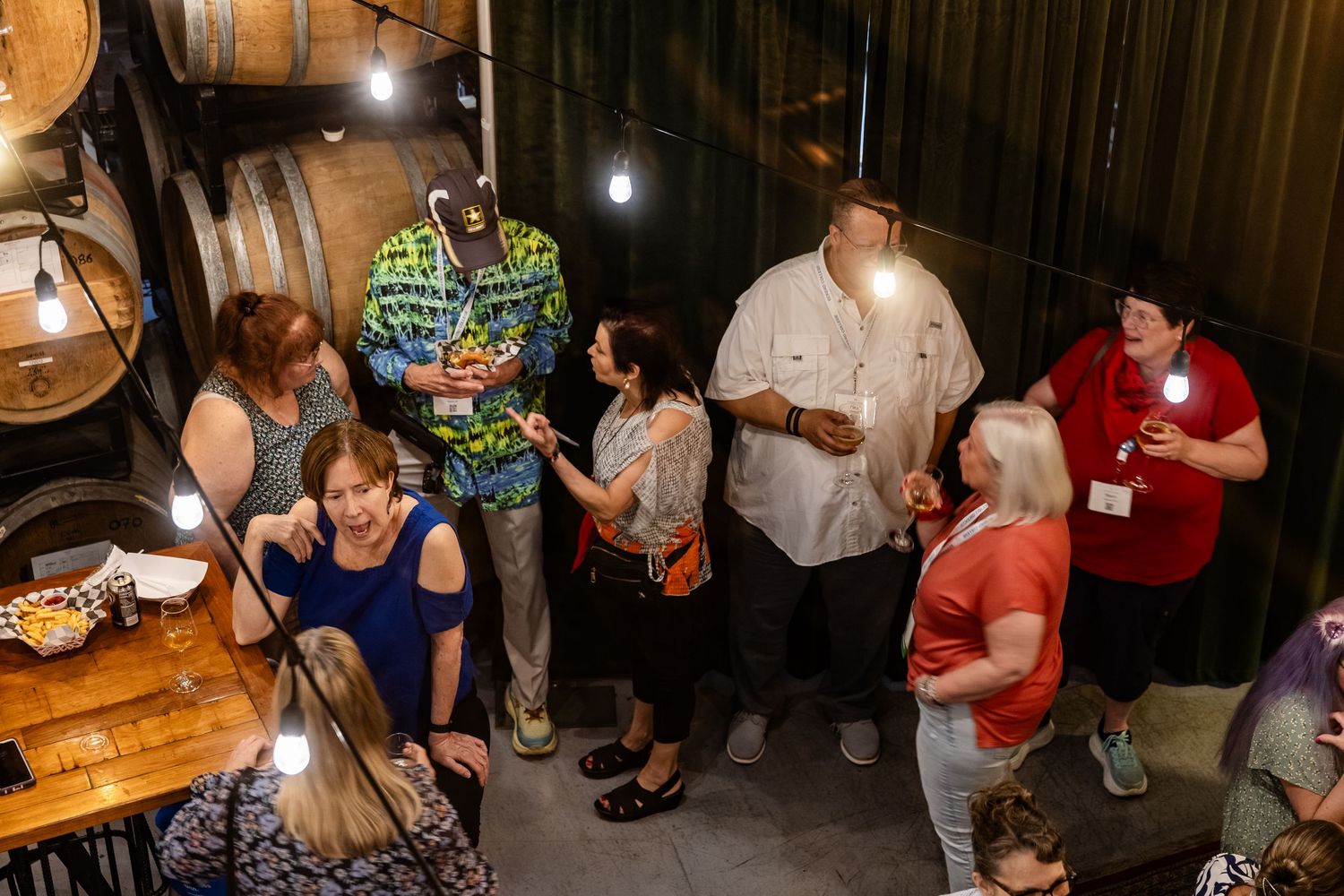 Groups of people mingling and socializing inside a rustic barrel-lined venue at a social event.