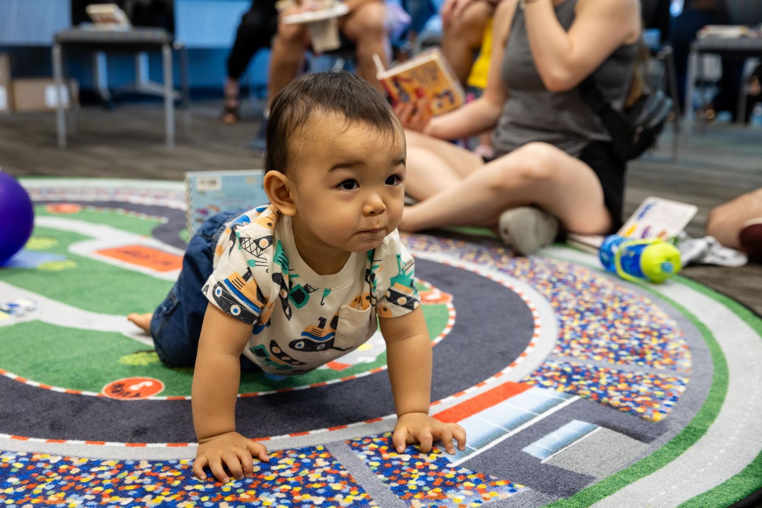 A curious baby crawls on a colorful road-themed rug during a children's activity session indoors.