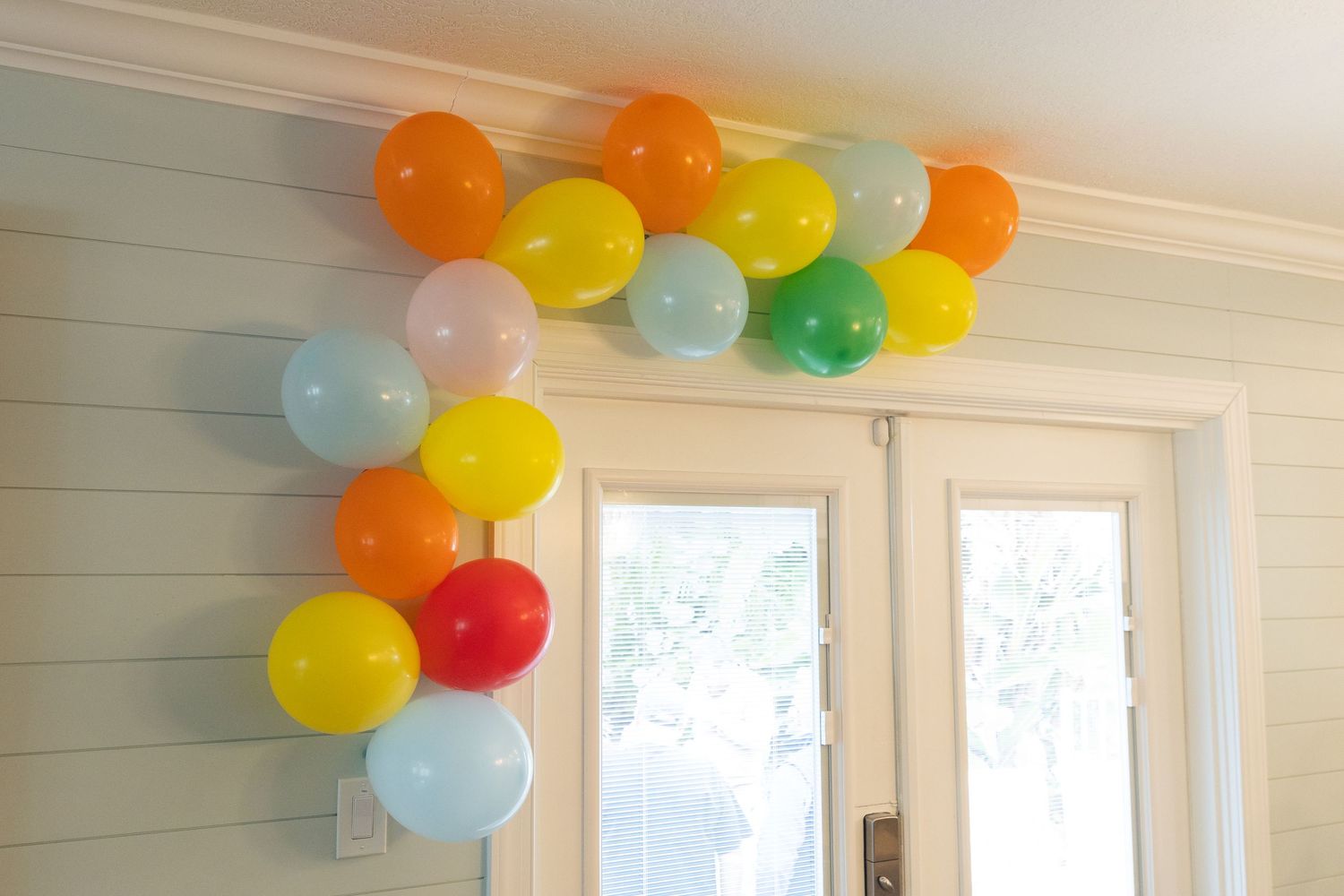 Colorful balloon garland arch with red, yellow, green, orange, and blue balloons decorating a white French door.