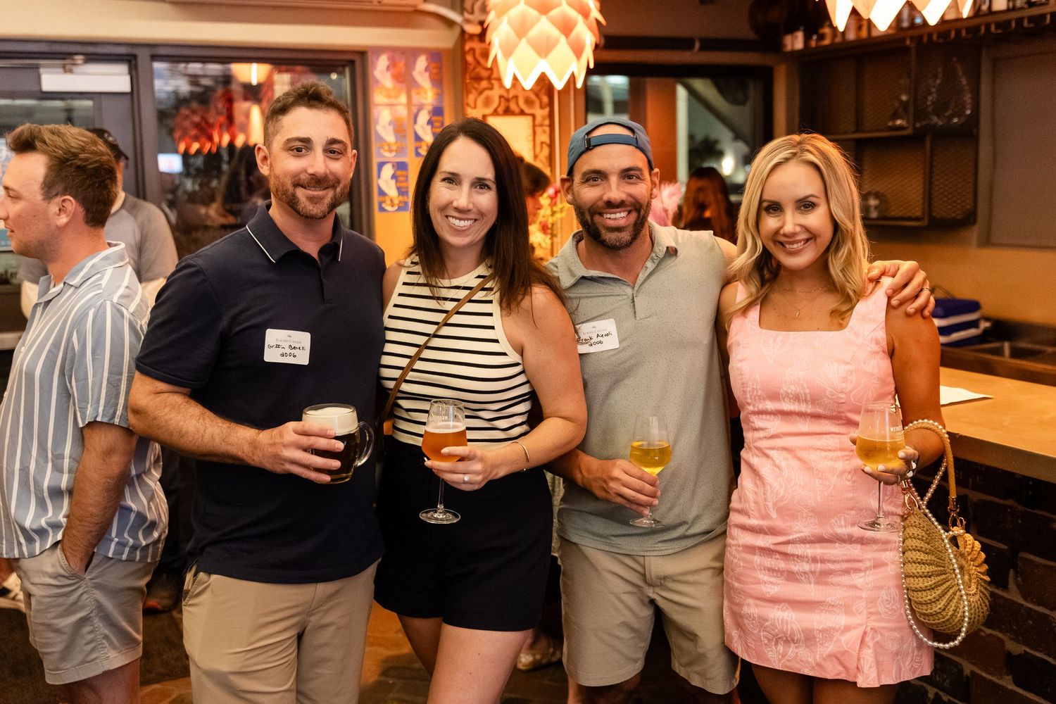 Four friends smiling and holding drinks at a casual indoor social gathering or happy hour event.