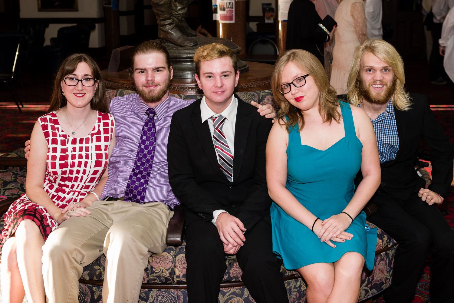 Five young adults posing together at a formal event, dressed in elegant attire including suits and dresses.