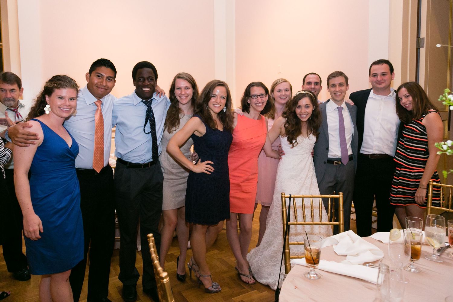 Diverse group of smiling wedding guests pose together for photo at elegant indoor reception venue.