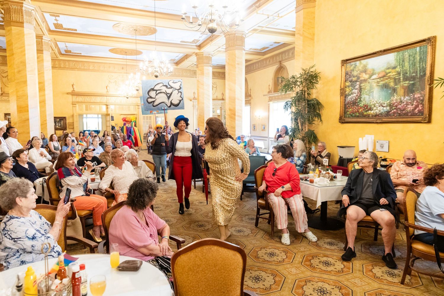 Guests gather in an elegant ballroom with ornate decor for a lively social event featuring a woman in red.