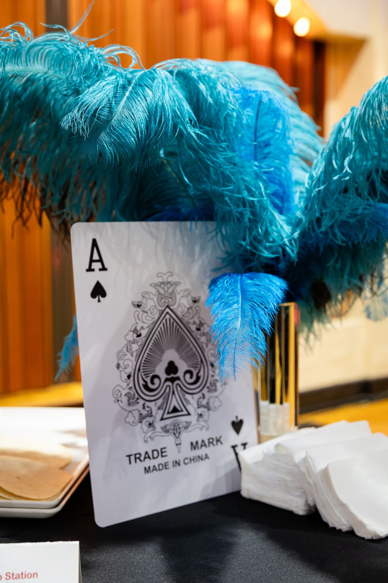 Ace of spades playing card displayed with blue ostrich feathers as casino themed table centerpiece.