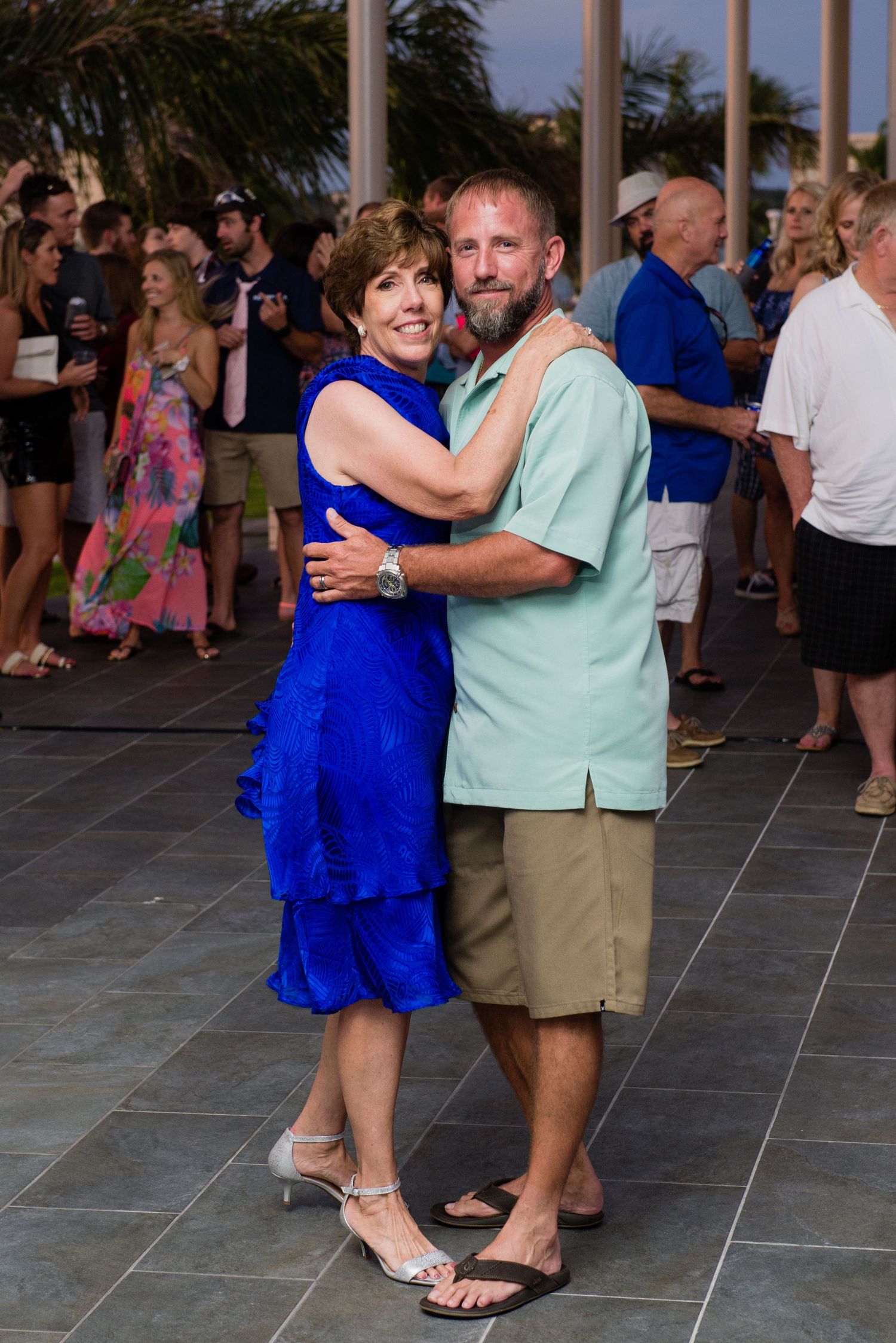 Couple dancing together at an outdoor wedding reception, woman in blue dress and man in green shirt.