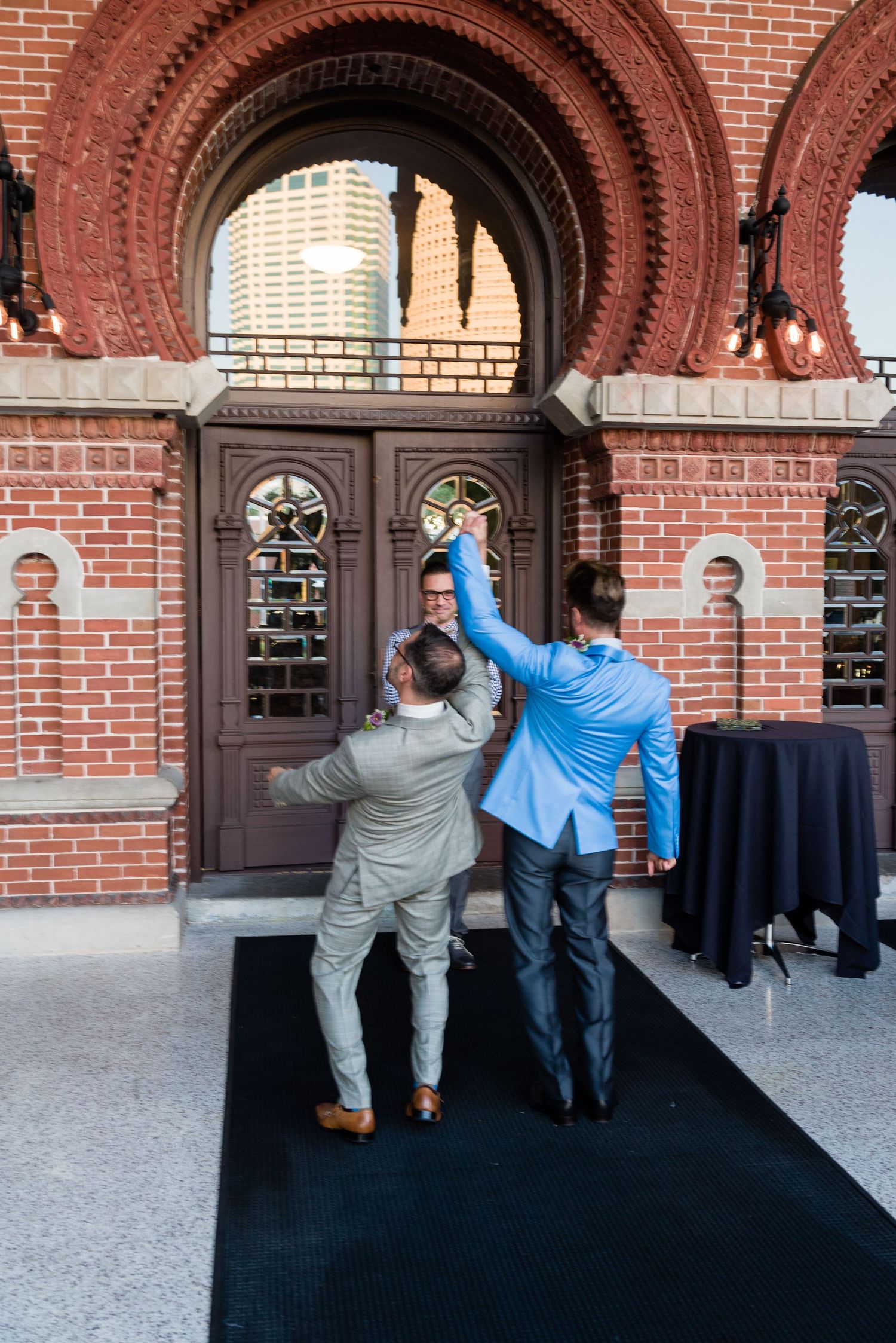 Two men high-fiving outside a historic red brick building with ornate arched doorway and stained glass windows.