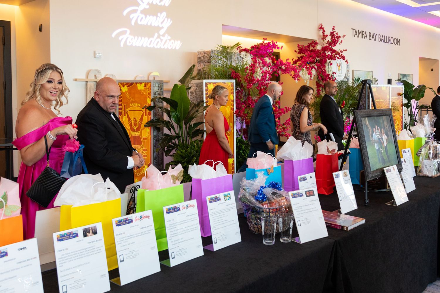 Elegant charity gala auction table with colorful gift bags at Tampa Bay Ballroom fundraising event.