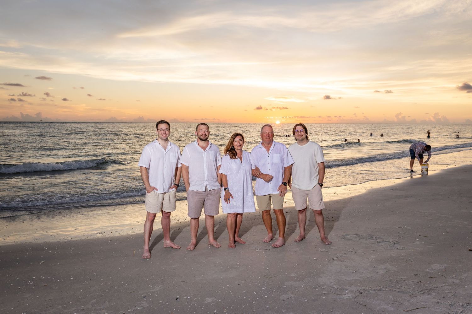 Family of five posing on beach at sunset wearing white outfits.